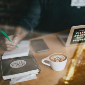 Cappuccino art on white ceramic mug beside a laptop.